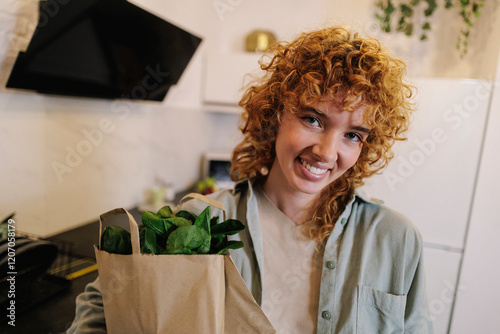 Smiling young woman holding groceries package delivered at home photo