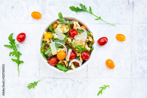 Pasta bowl with rocket, tomatoes, zucchini and red onion on a light background photo