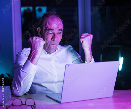 Excited mature freelancer celebrating on video call through laptop at home office photo