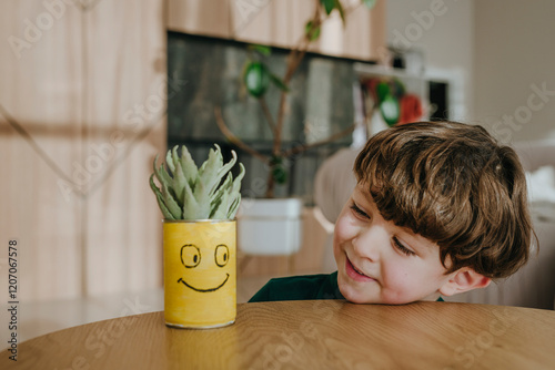 Cute boy looking at potted plant in home photo