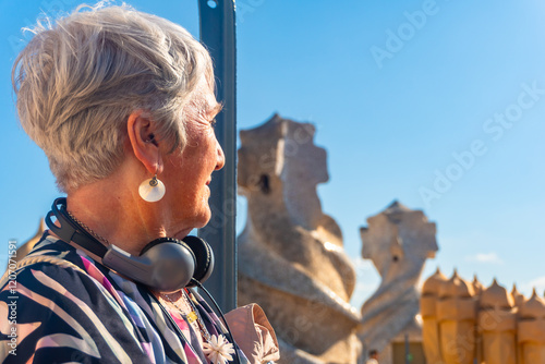 Fotografía Senior tourist woman wearing headphones exploring park guell in barcelona, catal