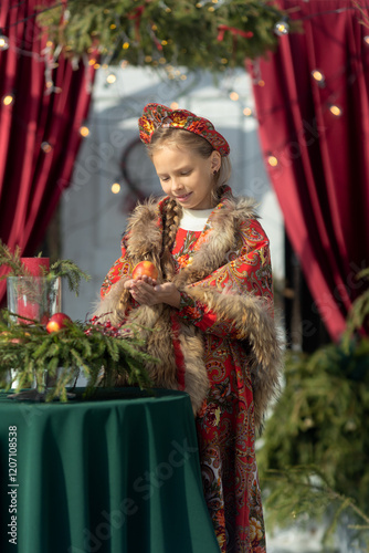 A blonde girl in a national Russian costume on the Maslenitsa holiday. A child in a traditional costume with fur trim and a headdress against a festive backdrop. Winter scene with a beautiful girl