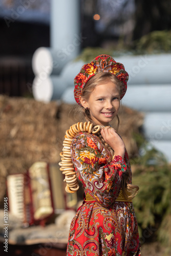 A blonde girl in a national Russian costume on the Maslenitsa holiday. A beautiful russian girl in a national costume made of a fur cape and kokoshnik on the background of a hayloft. 