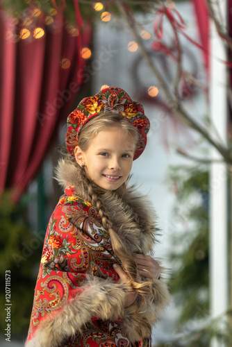 A blonde girl in a national Russian costume on the Maslenitsa holiday. A child in a traditional costume with fur trim and a headdress against a festive backdrop. Winter scene with a beautiful girl