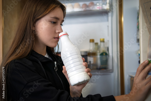 hungry girl open empty refrigerator. A girl sniffs an open bottle of milk. The girl takes out a white bottle of fresh milk from the refrigerator.