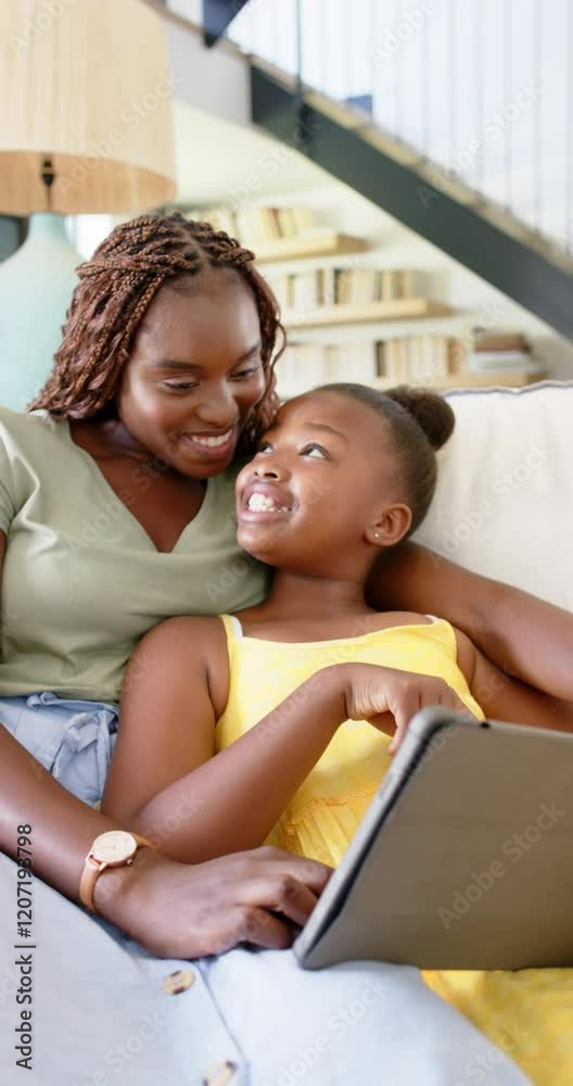Vertical video: Smiling mother and daughter using tablet together while relaxing on couch Vertical video: Smiling mother and daughter using tablet together while relaxing on couch