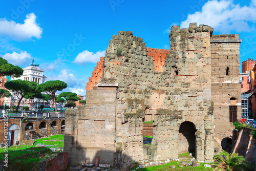 Obraz na płótnie Ancient ruins in Rome, Italy, featuring weathered stone walls under a vivid blue sky, surrounded by lush greenery and iconic umbrella pines. The Altare della Patria is visible in the background w salonie