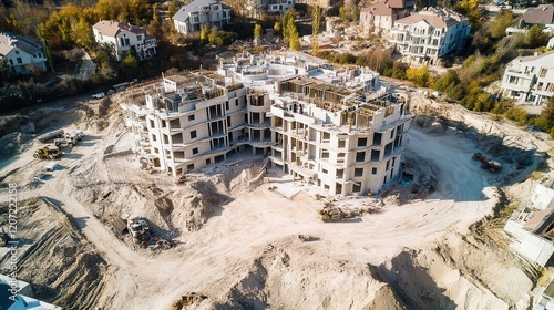 A vibrant construction site buzzes with activity as workers skillfully erect an elegant building amidst a serene residential backdrop.