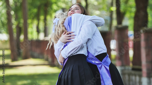 Two joyful female graduates hugging with sashes on their last day of school, commemorating their academic success photo