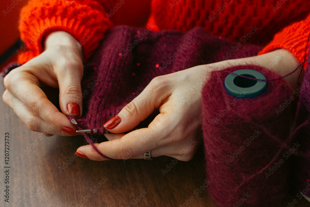 Women hands holding knitting needles and red knitted sweater with sequins. Knitting woman with bobbins of yarn and burgundy knitwear. Sequin pattern in needlework. Knitting hobby. Knitter work.