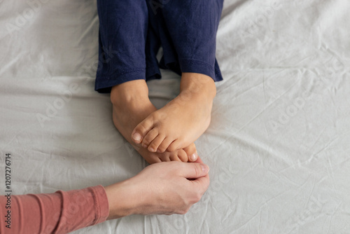 Mother tickling child's feet on bed. Playful bonding moment