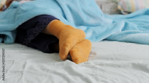 Feet of a child wearing yellow socks, sleeping under a soft blue blanket in bed