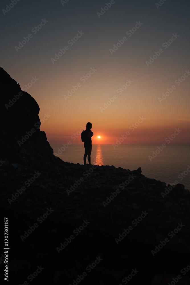 Fototapeta premium A hiker silhouetted against a glowing sunset over the Mediterranean in Mallorca.