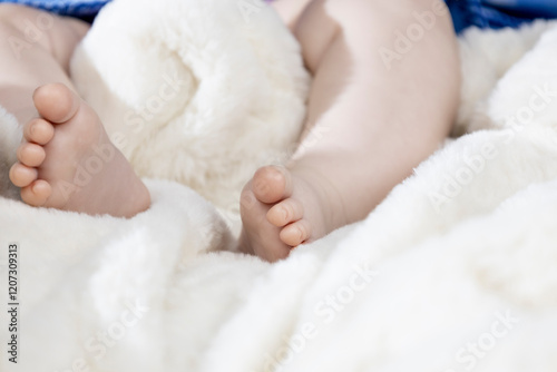 Legs infant baby lying on white bed.