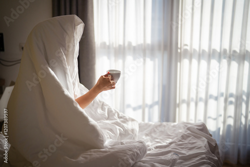 Woman with cup of coffee in the morning under the blanket at home