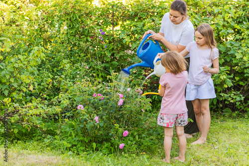Mother and daughters watering plants together in a summer garden