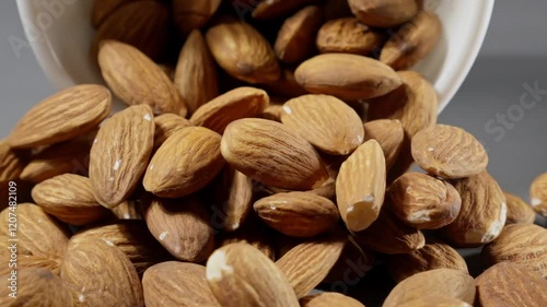 Falling almonds on grey background. Almond nuts fall on table. Close-up of brown almond nuts falling from white bowl on gray table. Pile of healthy food for vegan. Slow motion