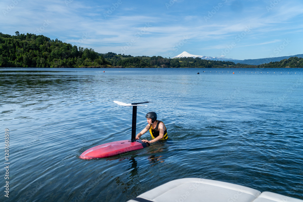 A teenager wearing a life jacket and helmet, floating in the lake alongside a foil board, getting ready for an exciting water sport adventure.