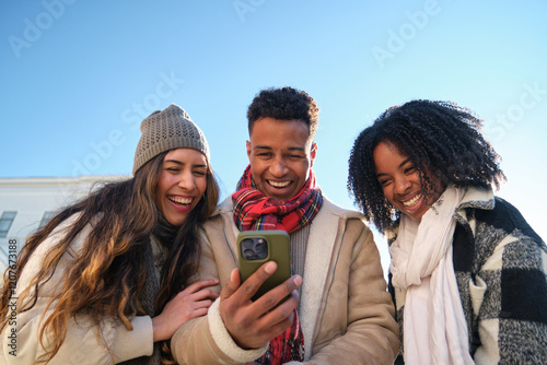 Obraz na płótnie Three young students are having fun watching something on a smartphone in winter w salonie