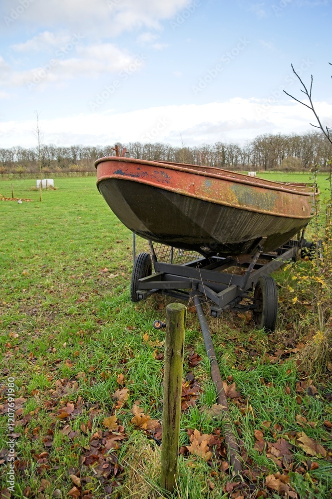 A neglected old rusty rowing boat on a trailer on the edge of a meadow. A neglected old rusty rowing boat on a trailer on the edge of a meadow.