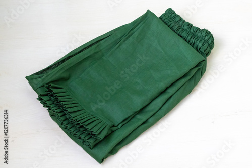 A green salwar, a traditional South Asian garment resembling loose-fitting pants, is folded and displayed against a light wooden backdrop. photo