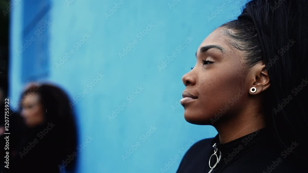 One contemplative black latina girl gazing upwards with HOPE and FAITH leaning on blue wall in urban street environment. African American young woman portrait looking up with thoughtful gaze