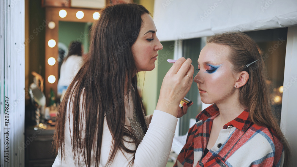 Skilled makeup artist applying bold, colorful eyeshadow on model's eyelids during professional beauty salon photoshoot Skilled makeup artist applying bold, colorful eyeshadow on model's eyelids during professional beauty salon photoshoot