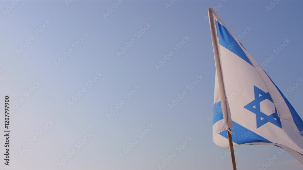 A tattered and torn Israeli flag flutters against the backdrop of the Mediterranean Sea and blue sky