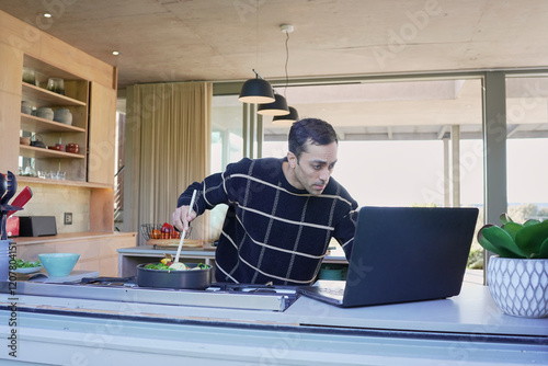 Man cooking and looking at laptop photo