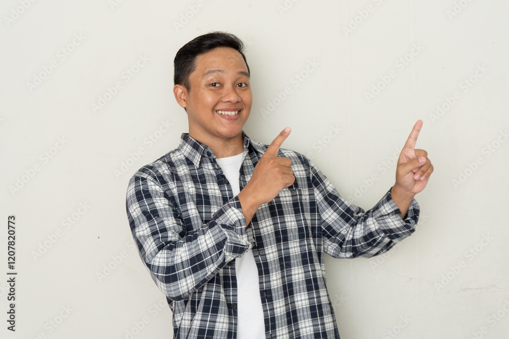 Attractive young Asian man smiling and pointing his finger to the side. Copy space. 