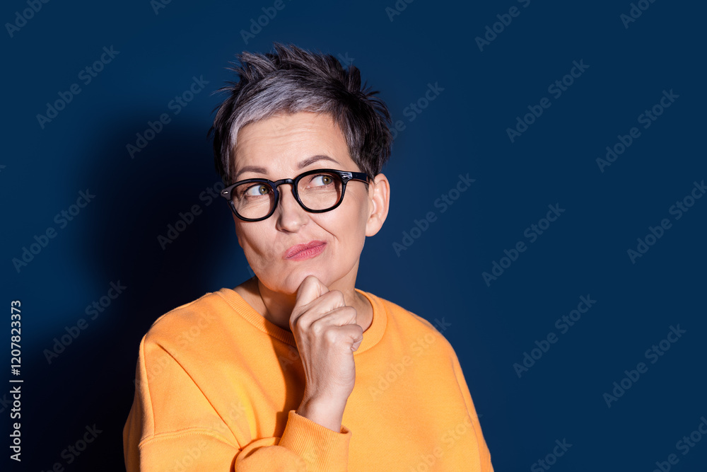 Photo portrait of pretty senior female look skeptical minded empty space wear trendy yellow outfit isolated on dark blue color background Photo portrait of pretty senior female look skeptical minded empty space wear trendy yellow outfit isolated on dark blue color background
