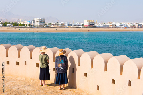 Two female tourists by crenelated wall of lighthouse, Al Ayjah village, Sur, capital of Ash Sharqiyah Region, Sultanate of Oman, Arabian Peninsula