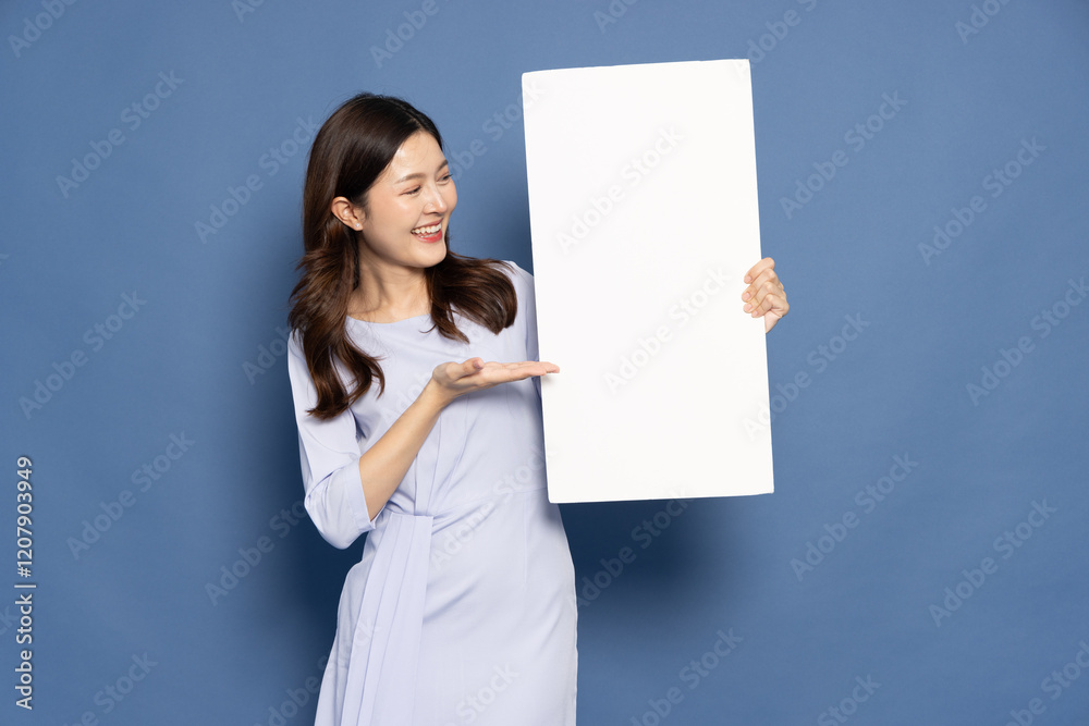 Young Asian businesswoman showing and holding blank white billboard banner for advertising isolated on blue background