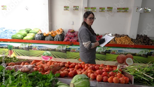 A woman in a fruit and vegetable supermarket is listing the inventory of tomatoes, carrots and other vegetables in the warehouse