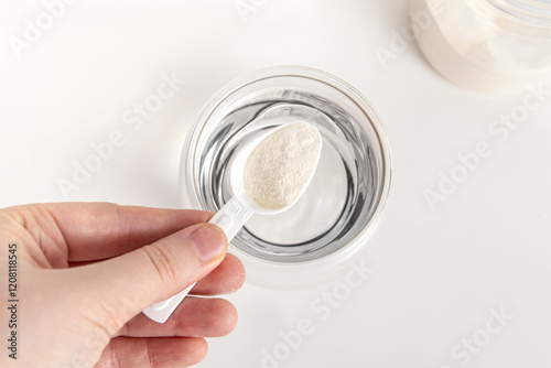 Woman pours a measuring spoon of powder into a glass of water. Protein or collagen