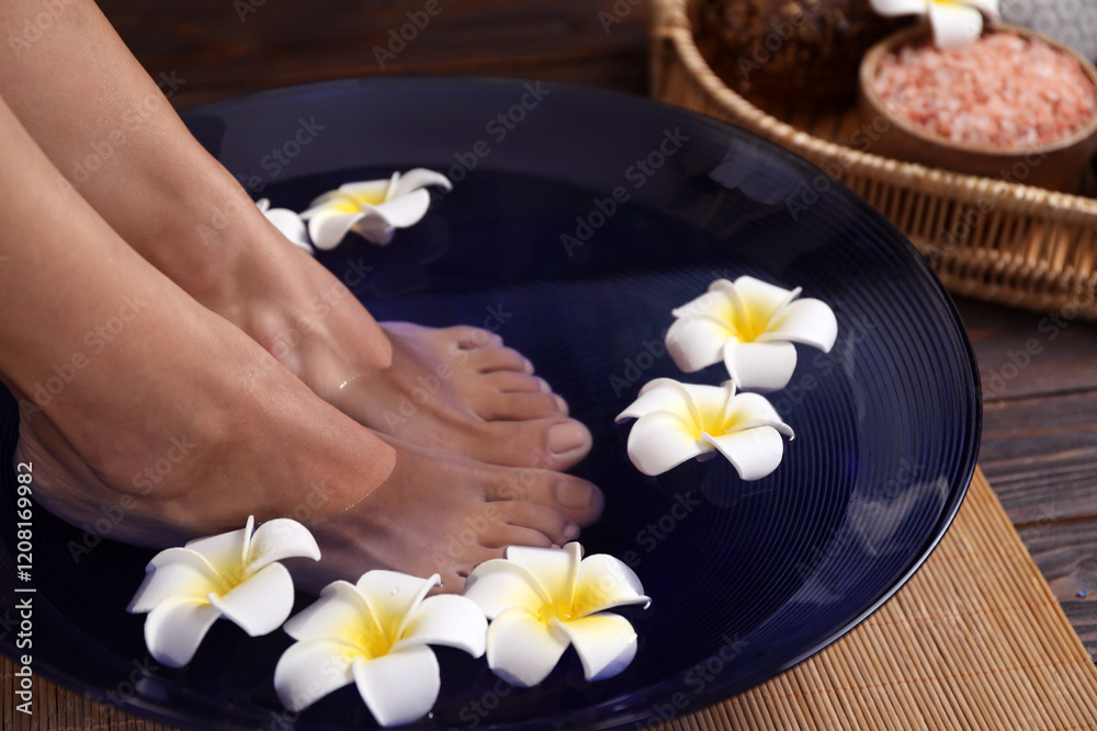 Woman soaking her feet in bowl with water and plumeria flowers on floor, closeup. Spa treatment Woman soaking her feet in bowl with water and plumeria flowers on floor, closeup. Spa treatment