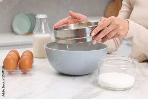 Making dough. Woman sifting flour into bowl at white table, closeup