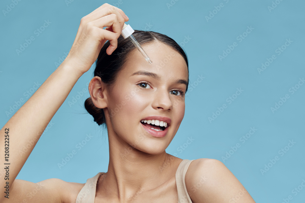 Young woman applying serum for radiant skin on a blue background, showcasing confidence and beauty in skincare