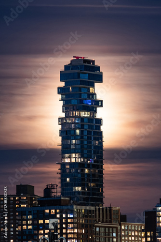 Striking nighttime view of the Jenga Tower at 56 Leonard Street in New York City, with its distinctive stacked design illuminated against a glowing, cloud-covered sky.
 photo