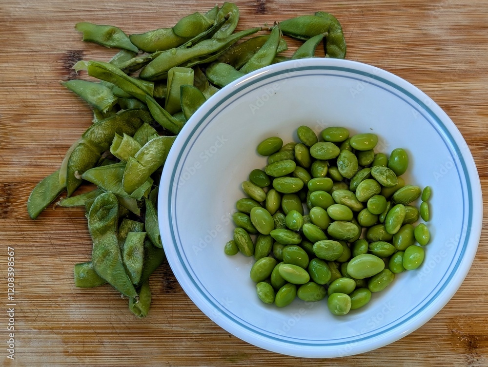 Fresh Shelled Edamame Beans in White Bowl with Empty Pods on Wooden Cutting Board Fresh Shelled Edamame Beans in White Bowl with Empty Pods on Wooden Cutting Board