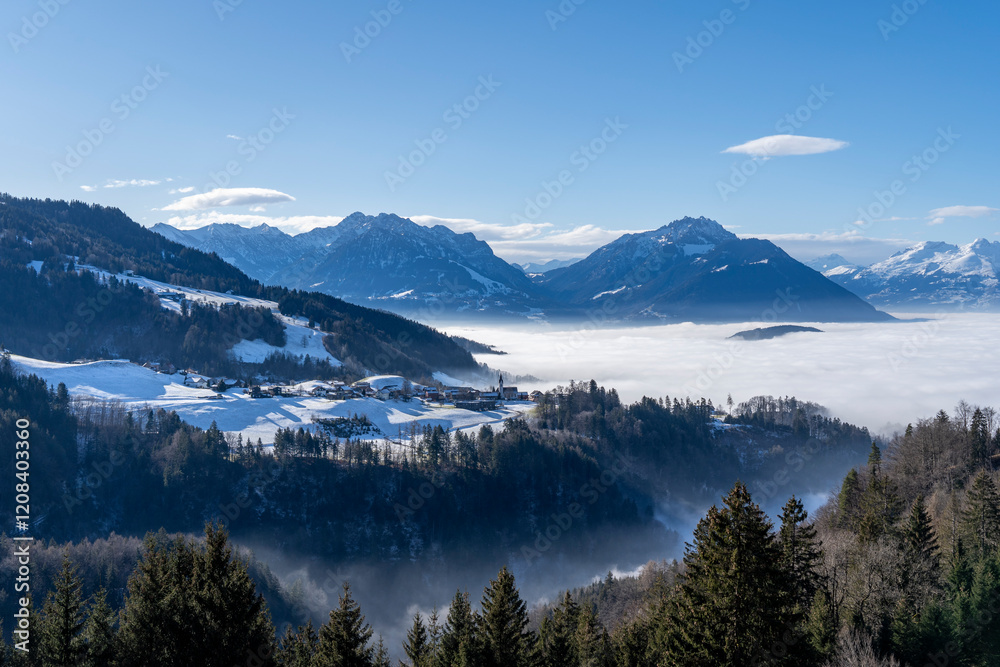 village of Furx in Vorarlberg surrounded by mountains in the snow but above the sea of fog towards blue sky village of Furx in Vorarlberg surrounded by mountains in the snow but above the sea of fog towards blue sky