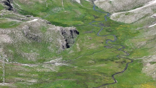 An aerial view of winding streams flowing through lush green meadows in a high-altitude landscape, showcasing the pristine beauty and tranquility of untouched nature