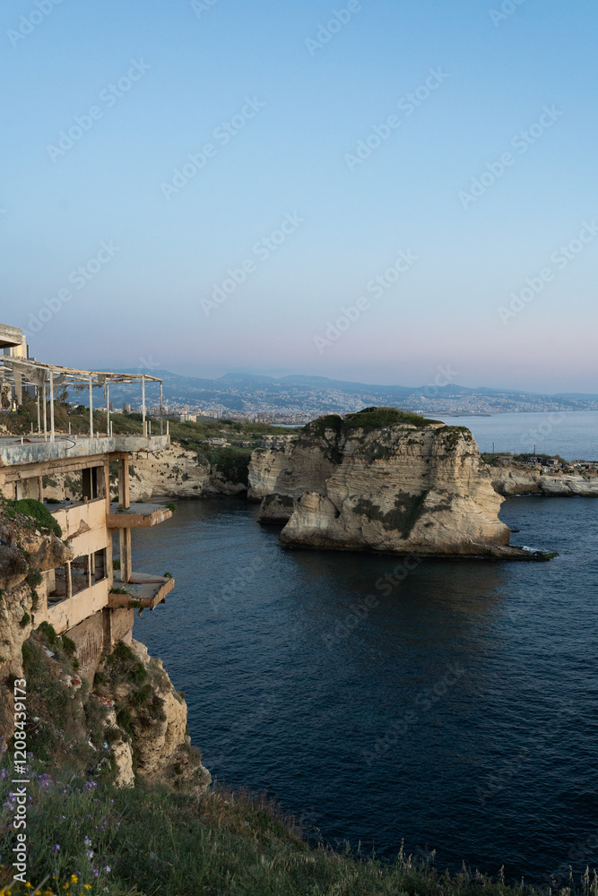 Fototapeta premium The sun sets behind Raouche Rock in Lebanon, casting a stunning glow over the Mediterranean waters. Travel agencies, wallpapers, and social media content.