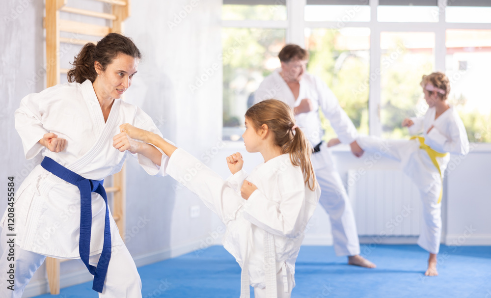 Focused preteen girl in white kimono practicing karate kicking techniques during sparring with mother. Sports family activity concept..