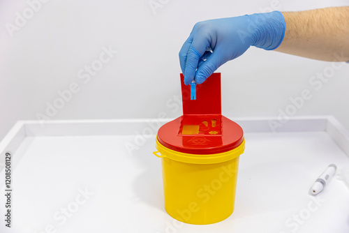 Old medicine syringes thrown into a medical waste container. The syringe is placed in the medical waste bin. A red-lidded hazardous material bin. Needles being put ito a sharps bin. photo