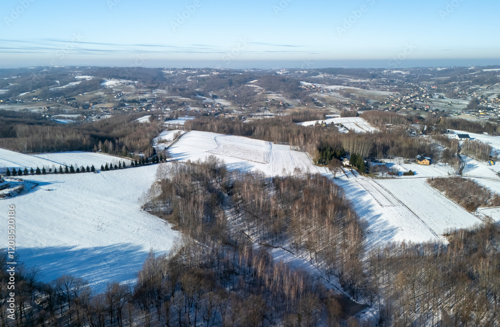 Aerial view of a serene winter landscape with snow-covered hills and bare trees under a clear blue sky. Aerial view of a serene winter landscape with snow-covered hills and bare trees under a clear blue sky.
