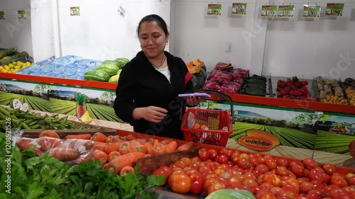 A domestic worker is buying some carrots in a fruit and vegetable store, she has a basket in her hand and two carrots in the other hand