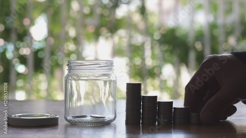 A person hand putting money coin into a glass jar filled with coins. Investment and Interest concept video, plant growing background in the saving coin, coin in the jar.