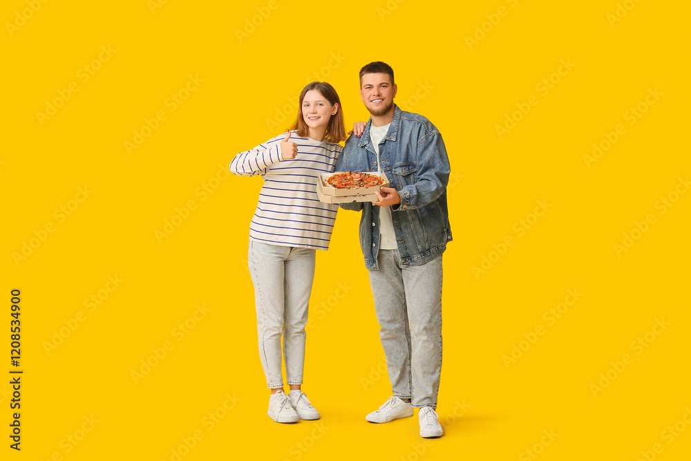 Beautiful young happy couple with cardboard box of tasty pizza showing thumb-up gesture on yellow background Beautiful young happy couple with cardboard box of tasty pizza showing thumb-up gesture on yellow background