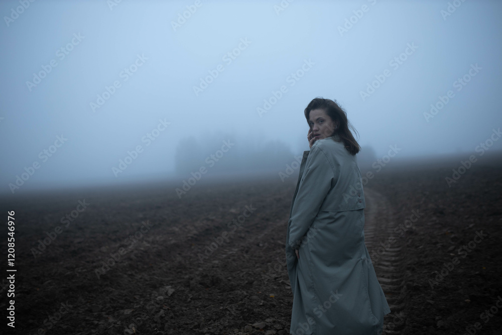 gloomy woman in coat walks alone in foggy field, existential crisis
